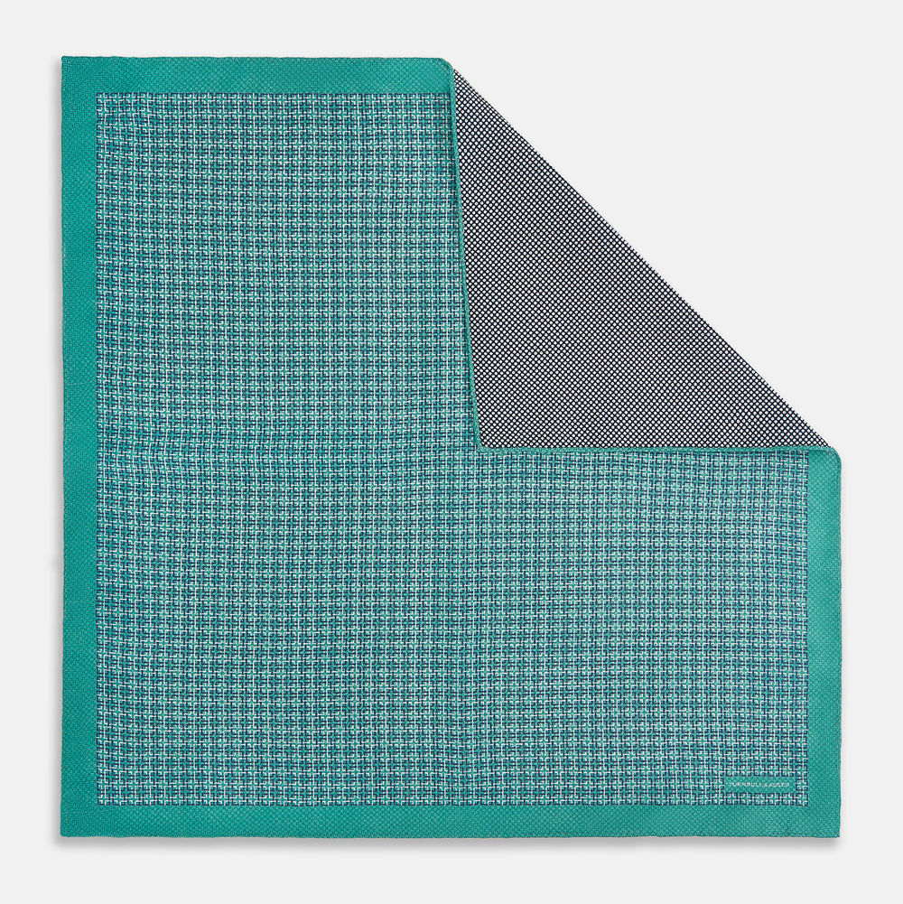 A geometric green silk pocket square by Turnbull & Asser UK, featuring a subtle houndstooth weave with a teal border, and partially folded to reveal a contrasting black and white micro-dot reverse pattern.