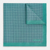 View 2 of product A geometric green silk pocket square by Turnbull & Asser UK, featuring a subtle houndstooth weave with a teal border, and partially folded to reveal a contrasting black and white micro-dot reverse pattern.