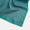 View 3 of product A geometric green silk pocket square by Turnbull & Asser UK, featuring a subtle houndstooth weave with a teal border, and partially folded to reveal a contrasting black and white micro-dot reverse pattern.