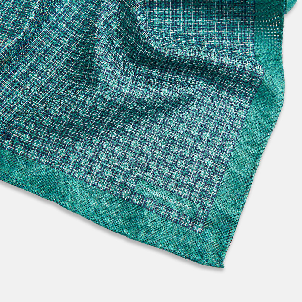 A geometric green silk pocket square by Turnbull & Asser UK, featuring a subtle houndstooth weave with a teal border, and partially folded to reveal a contrasting black and white micro-dot reverse pattern.