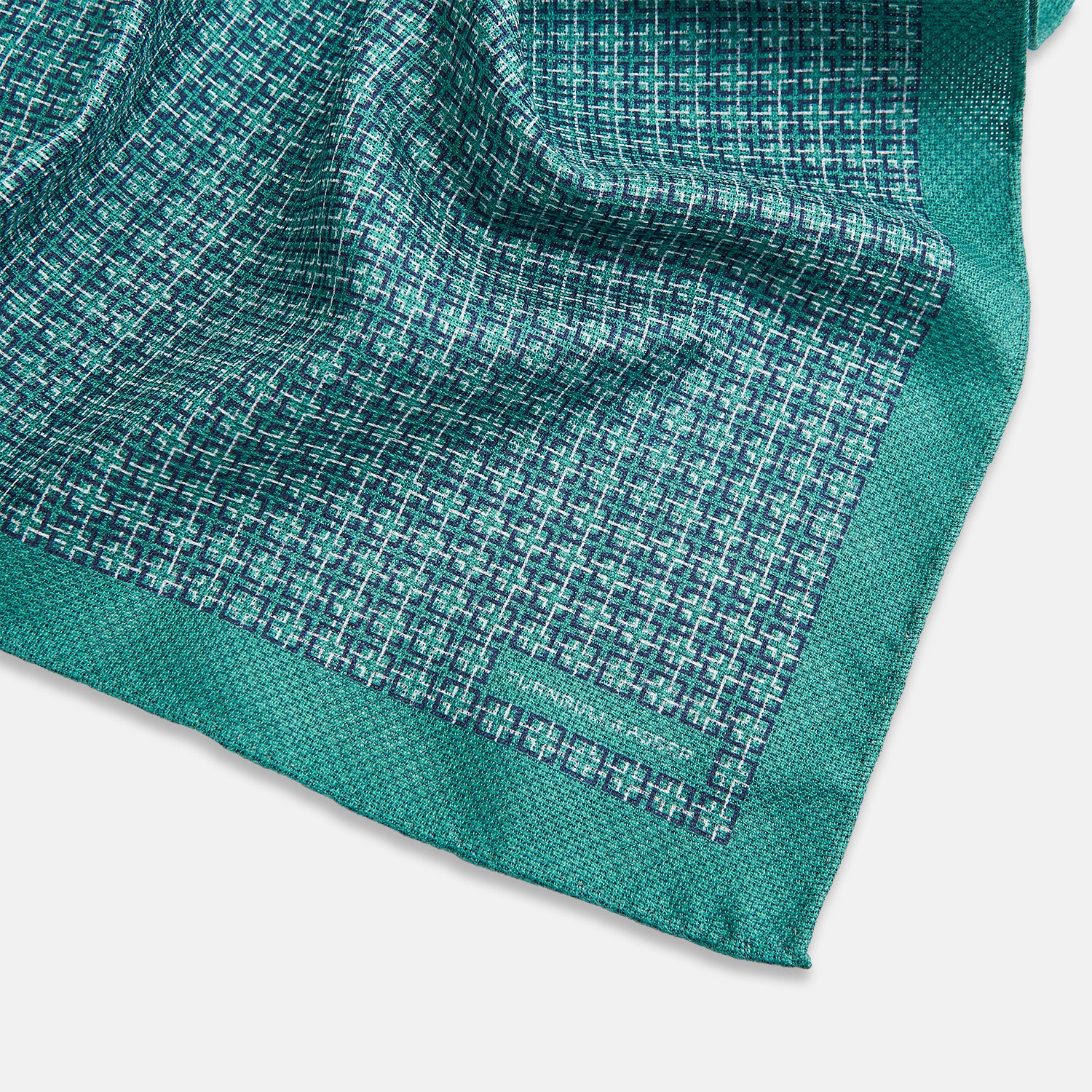 View 3 of product A geometric green silk pocket square by Turnbull & Asser UK, featuring a subtle houndstooth weave with a teal border, and partially folded to reveal a contrasting black and white micro-dot reverse pattern.