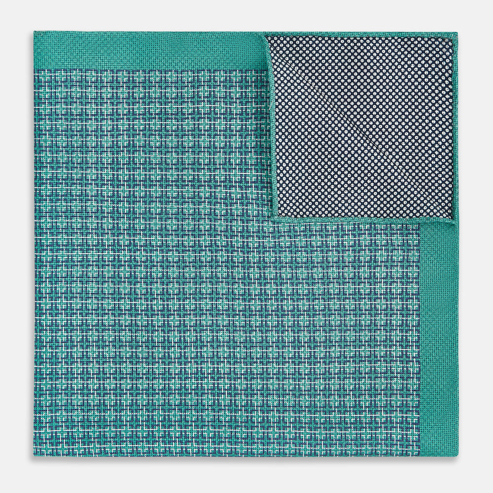 A geometric green silk pocket square by Turnbull & Asser UK, featuring a subtle houndstooth weave with a teal border, and partially folded to reveal a contrasting black and white micro-dot reverse pattern.