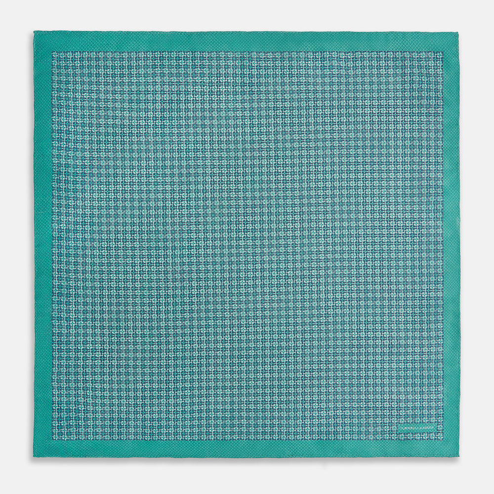 A geometric green silk pocket square by Turnbull & Asser UK, featuring a subtle houndstooth weave with a teal border, and partially folded to reveal a contrasting black and white micro-dot reverse pattern.