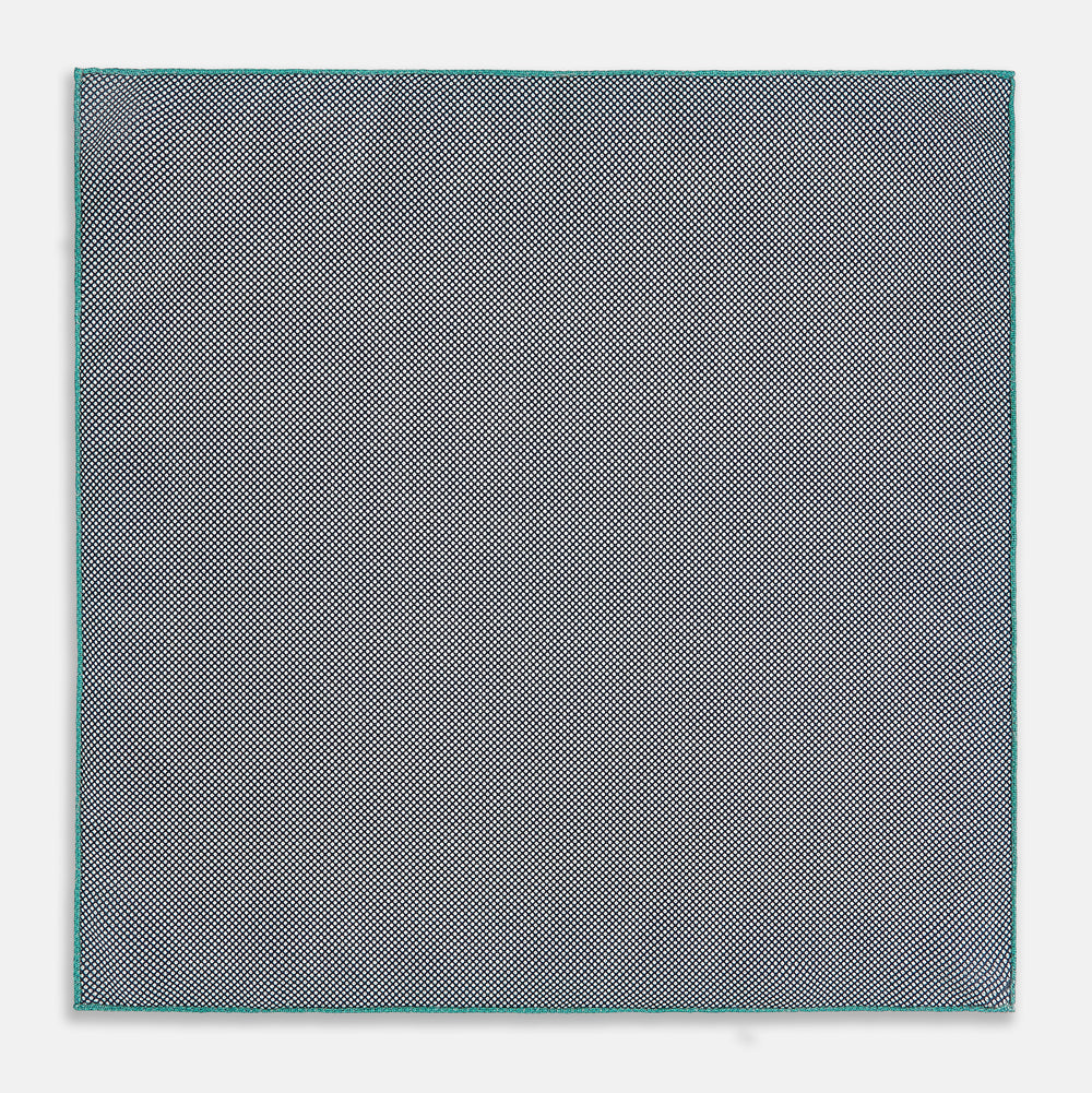 A geometric green silk pocket square by Turnbull & Asser UK, featuring a subtle houndstooth weave with a teal border, and partially folded to reveal a contrasting black and white micro-dot reverse pattern.