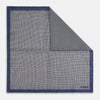 View 1 of product The Geometric Blue Pocket Square in Silk from Turnbull & Asser UK showcases a blue border and double-sided design, with a geometric pattern at the center. A folded corner reveals a refined, tighter dot motif on the reverse side, emphasizing the intricate craftsmanship of this finely woven accessory.