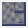 View 2 of product The Geometric Blue Pocket Square in Silk from Turnbull & Asser UK showcases a blue border and double-sided design, with a geometric pattern at the center. A folded corner reveals a refined, tighter dot motif on the reverse side, emphasizing the intricate craftsmanship of this finely woven accessory.