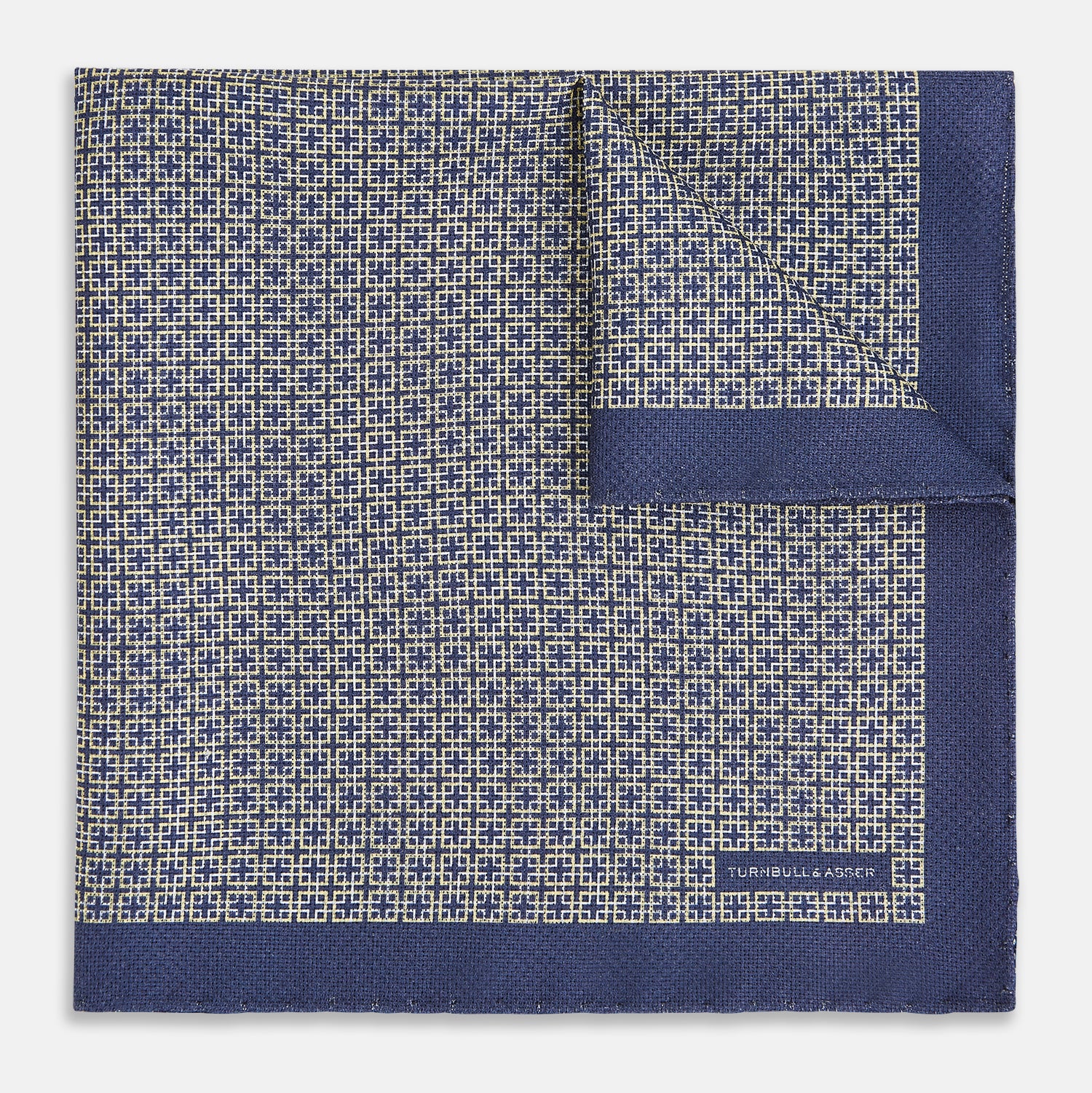 View 2 of product The Geometric Blue Pocket Square in Silk from Turnbull & Asser UK showcases a blue border and double-sided design, with a geometric pattern at the center. A folded corner reveals a refined, tighter dot motif on the reverse side, emphasizing the intricate craftsmanship of this finely woven accessory.