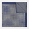 View 4 of product The Geometric Blue Pocket Square in Silk from Turnbull & Asser UK showcases a blue border and double-sided design, with a geometric pattern at the center. A folded corner reveals a refined, tighter dot motif on the reverse side, emphasizing the intricate craftsmanship of this finely woven accessory.