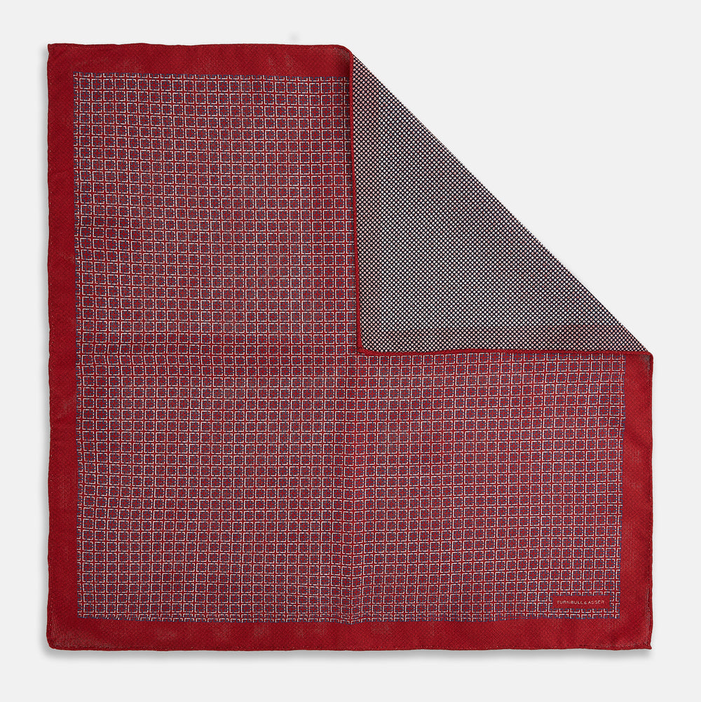 Turnbull & Asser UK’s Geometric Red Pocket Square in Silk features a small white checkered pattern and a cleverly flipped corner to showcase its contrasting black and white micro-dot reverse design.