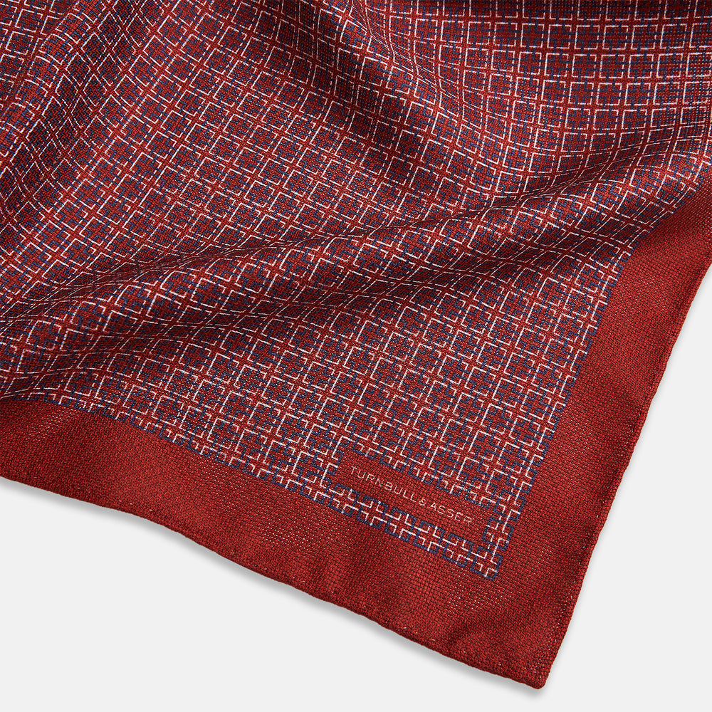 Turnbull & Asser UK’s Geometric Red Pocket Square in Silk features a small white checkered pattern and a cleverly flipped corner to showcase its contrasting black and white micro-dot reverse design.