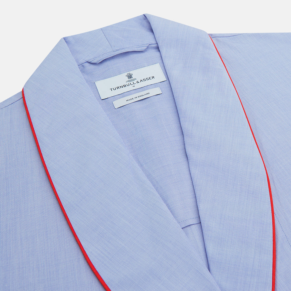 The Turnbull & Asser Light Blue Piped End-On-End Cotton Gown features a belted waist, three front pockets, and red piping on the collar, pockets, and cuffs—ideal for travel. Displayed against a white background.