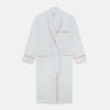 View 1 of product The Turnbull & Asser White Piped Herringbone Cotton Gown features long sleeves, a waist tie, chest pocket, and striking red piping on the collar, cuffs, pocket, and edges—an elegant piece showcased against a white background.
