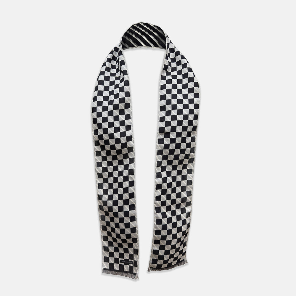 The Chequered Navy on White Frame Small Scarf in Silk by Turnbull & Asser UK is a long silk accessory featuring a classic black and white checkerboard pattern laid flat against a white background. Its ends are finished with a thin, fringed border, while the top edge is accented by diagonal stripes. The double-sided chequered design adds a stylish twist, with touches of navy and subtle hints of white bringing sophisticated detail to this timeless look.