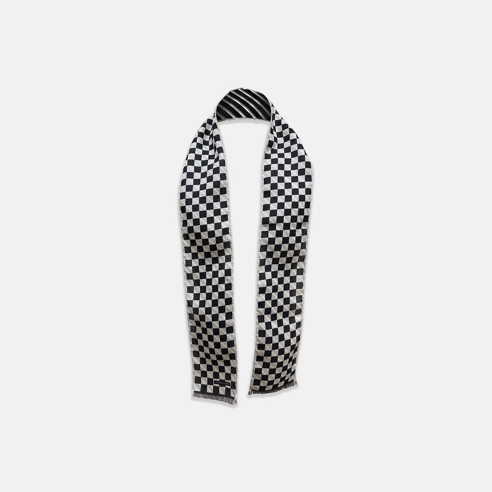 The Chequered Navy on White Frame Small Scarf in Silk by Turnbull & Asser UK is a long silk accessory featuring a classic black and white checkerboard pattern laid flat against a white background. Its ends are finished with a thin, fringed border, while the top edge is accented by diagonal stripes. The double-sided chequered design adds a stylish twist, with touches of navy and subtle hints of white bringing sophisticated detail to this timeless look.
