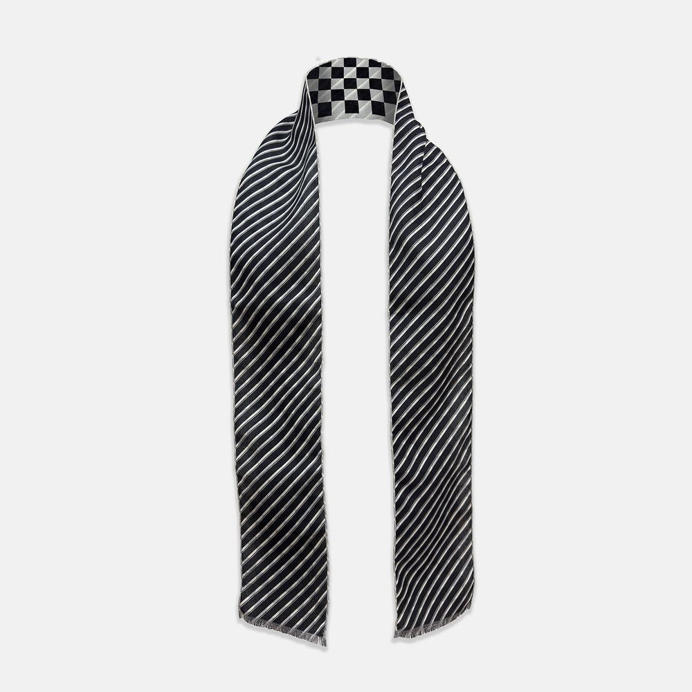The Chequered Navy on White Frame Small Scarf in Silk by Turnbull & Asser UK is a long silk accessory featuring a classic black and white checkerboard pattern laid flat against a white background. Its ends are finished with a thin, fringed border, while the top edge is accented by diagonal stripes. The double-sided chequered design adds a stylish twist, with touches of navy and subtle hints of white bringing sophisticated detail to this timeless look.