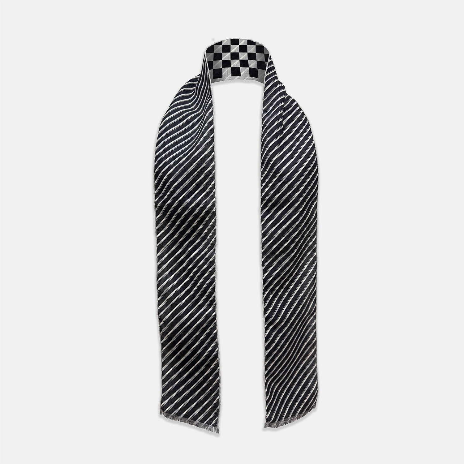 View 2 of product The Chequered Navy on White Frame Small Scarf in Silk by Turnbull & Asser UK is a long silk accessory featuring a classic black and white checkerboard pattern laid flat against a white background. Its ends are finished with a thin, fringed border, while the top edge is accented by diagonal stripes. The double-sided chequered design adds a stylish twist, with touches of navy and subtle hints of white bringing sophisticated detail to this timeless look.