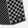 View 3 of product The Chequered Navy on White Frame Small Scarf in Silk by Turnbull & Asser UK is a long silk accessory featuring a classic black and white checkerboard pattern laid flat against a white background. Its ends are finished with a thin, fringed border, while the top edge is accented by diagonal stripes. The double-sided chequered design adds a stylish twist, with touches of navy and subtle hints of white bringing sophisticated detail to this timeless look.