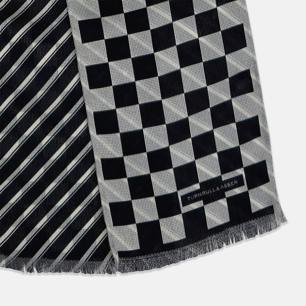 The Chequered Navy on White Frame Small Scarf in Silk by Turnbull & Asser UK is a long silk accessory featuring a classic black and white checkerboard pattern laid flat against a white background. Its ends are finished with a thin, fringed border, while the top edge is accented by diagonal stripes. The double-sided chequered design adds a stylish twist, with touches of navy and subtle hints of white bringing sophisticated detail to this timeless look.