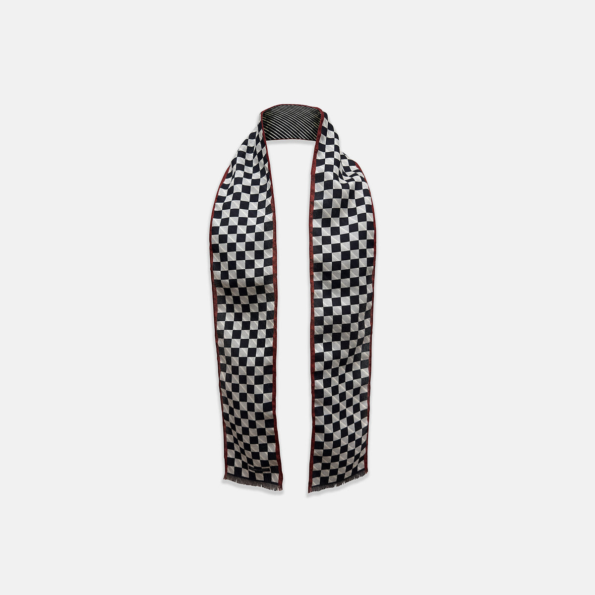 View 1 of product Introducing the Chequered Navy on Red Frame Small Scarf in Silk by Turnbull & Asser UK—a luxurious silk accessory featuring a navy and white chequered pattern, accented with thin red borders and delicate fringe at each end. Displayed against a white background, this scarf pays homage to British motoring heritage and the enduring elegance of Concours style.