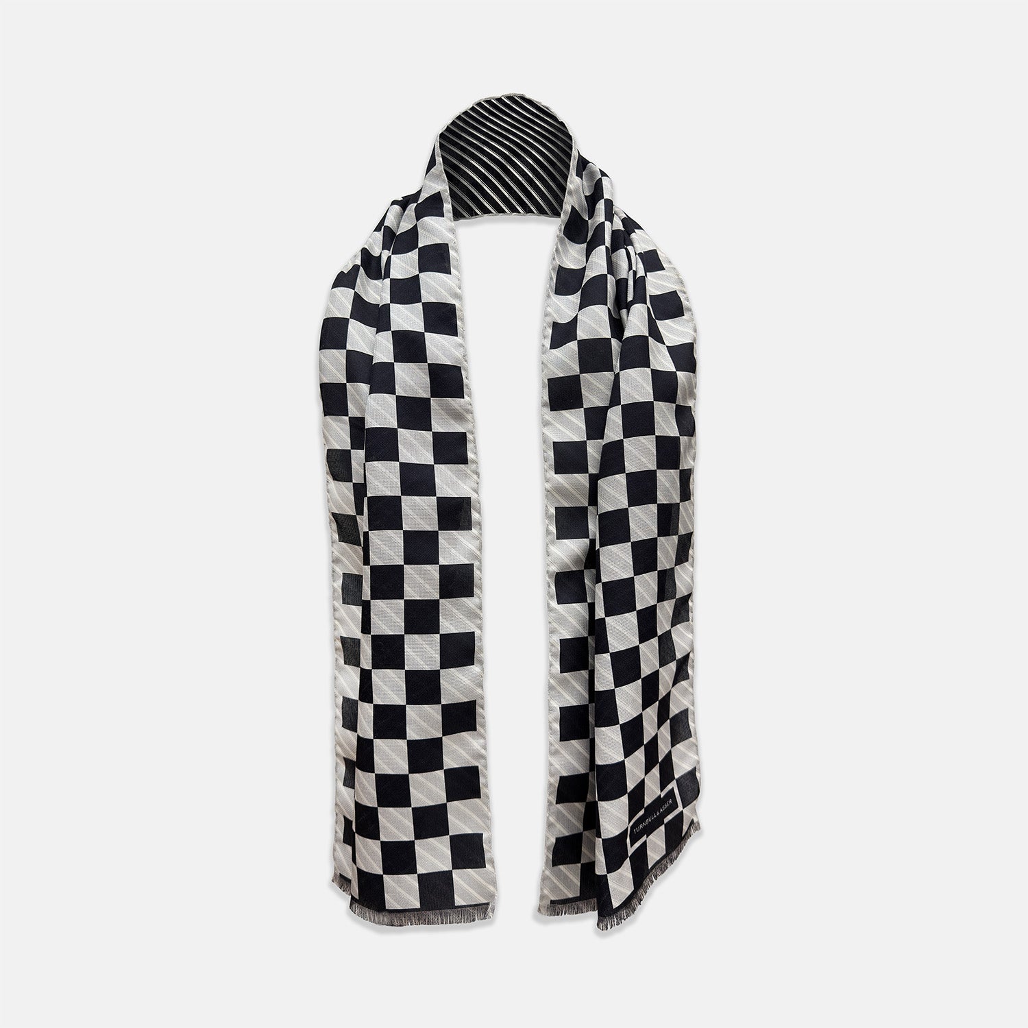 View 1 of product A Chequered Navy on White Frame Large Scarf in Silk from Turnbull & Asser UK, featuring a striking navy and white checkerboard motif inspired by classic British motoring heritage, is gracefully displayed over an invisible stand with its ends cascading downward and the top artfully folded into a striped semicircle—an impeccable choice for making a stylish statement at the Concours of Elegance 2026.