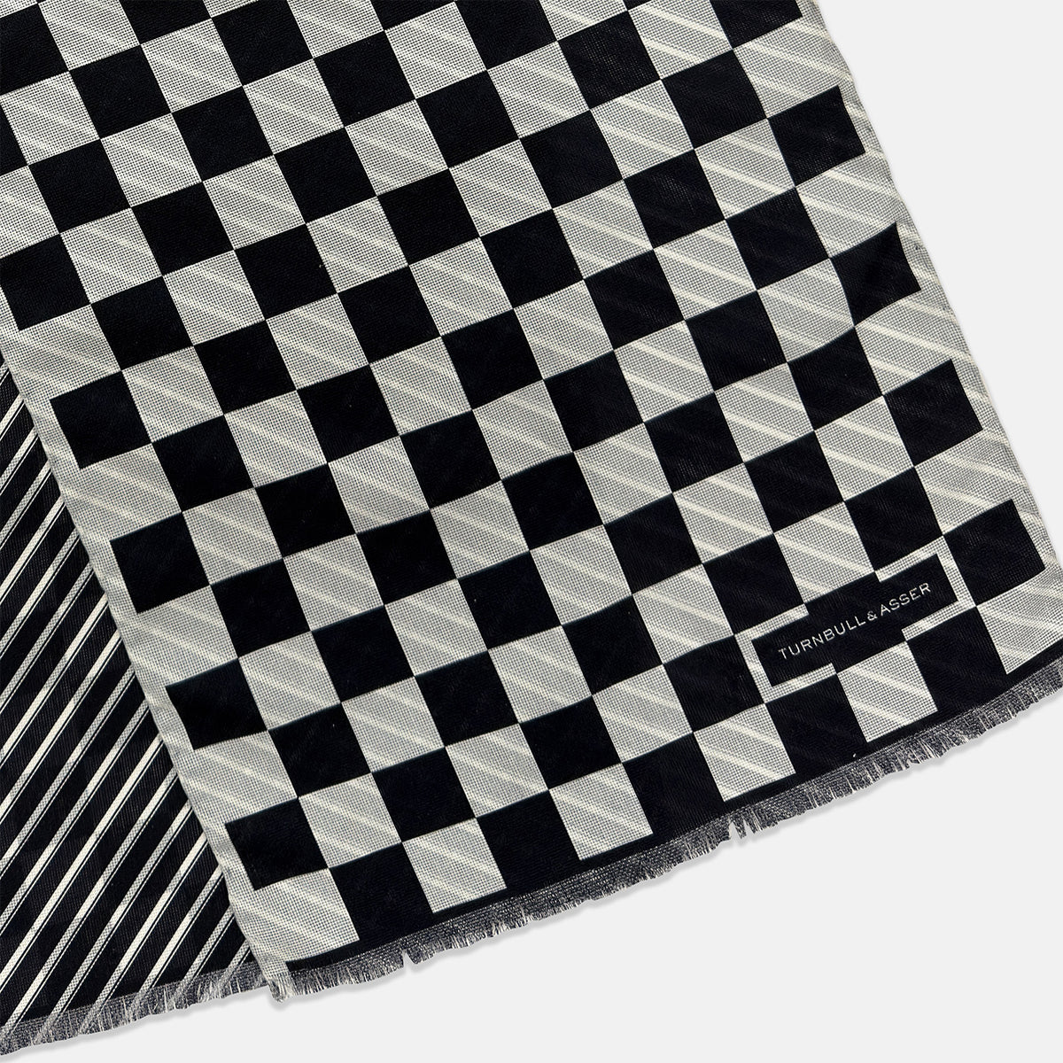 View 3 of product A Chequered Navy on White Frame Large Scarf in Silk from Turnbull & Asser UK, featuring a striking navy and white checkerboard motif inspired by classic British motoring heritage, is gracefully displayed over an invisible stand with its ends cascading downward and the top artfully folded into a striped semicircle—an impeccable choice for making a stylish statement at the Concours of Elegance 2026.