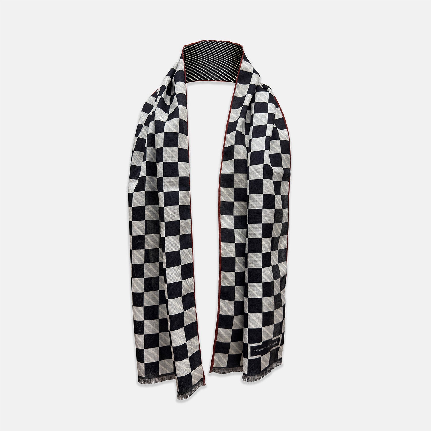 View 1 of product Chequered Navy on Red Frame Large Scarf in Silk by Turnbull & Asser UK, featuring a classic navy and white checkered pattern with a bold red border, elegantly displayed with both ends draped down to reveal the contrasting striped neck detail—a sophisticated nod to British motoring style, perfect for elevating your Concours of Elegance 2026 attire.