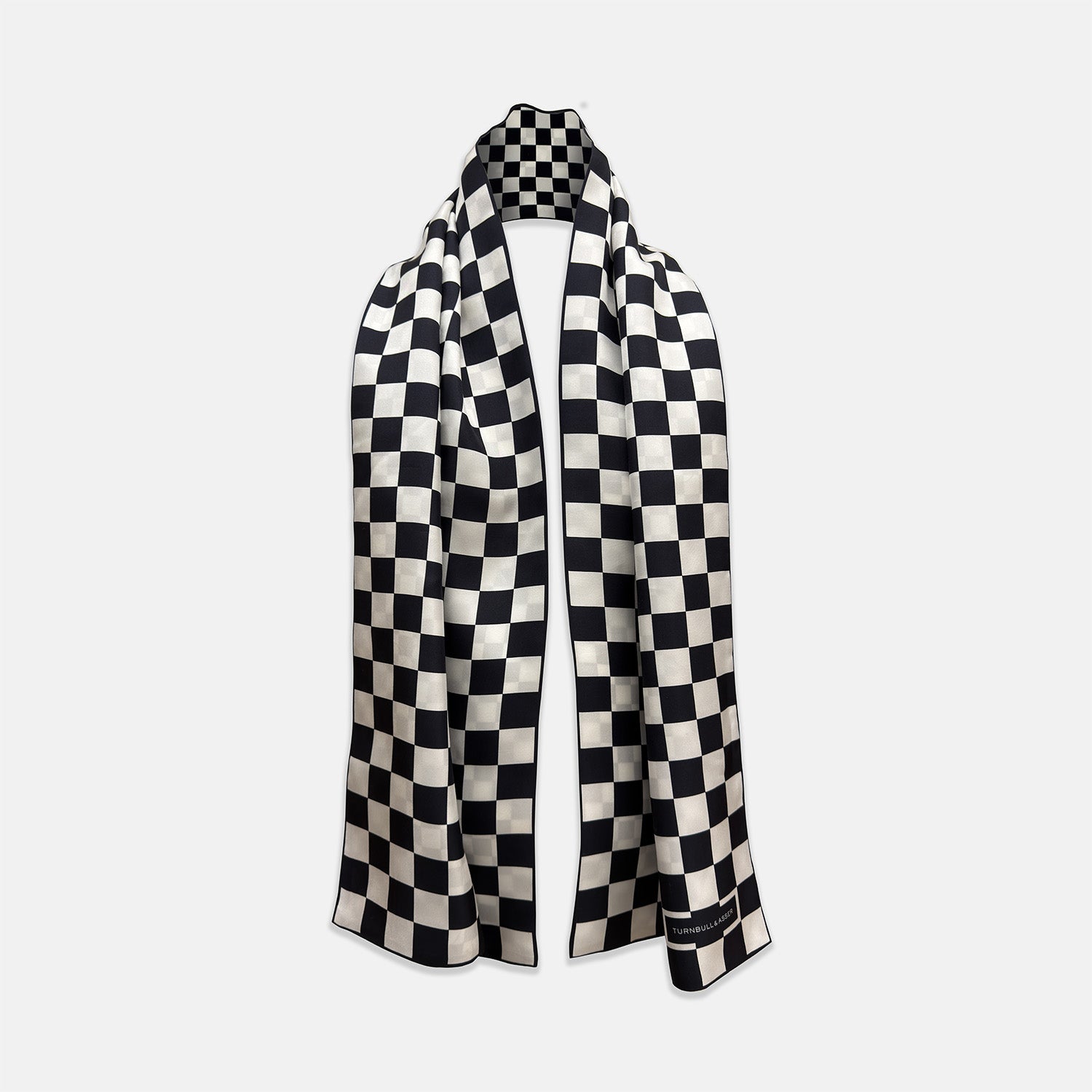 View 1 of product A Chequered Navy & White Scarf in Silk by Turnbull & Asser UK is displayed against a plain white background, showcasing its long, luxurious silk fabric with a striking navy and white checkered pattern.