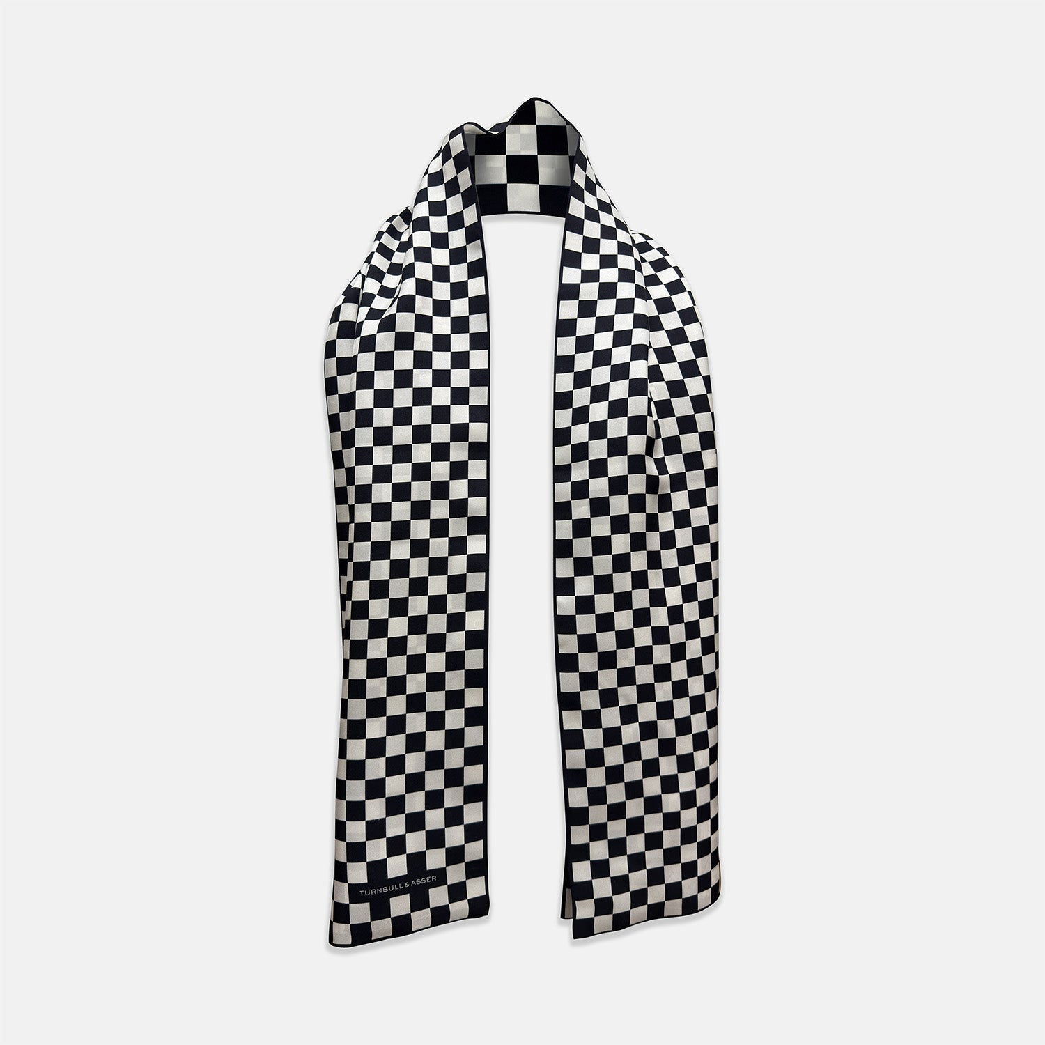 View 2 of product A Chequered Navy & White Scarf in Silk by Turnbull & Asser UK is displayed against a plain white background, showcasing its long, luxurious silk fabric with a striking navy and white checkered pattern.