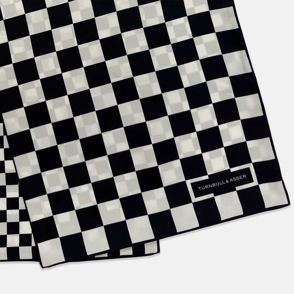 A Chequered Navy & White Scarf in Silk by Turnbull & Asser UK is displayed against a plain white background, showcasing its long, luxurious silk fabric with a striking navy and white checkered pattern.