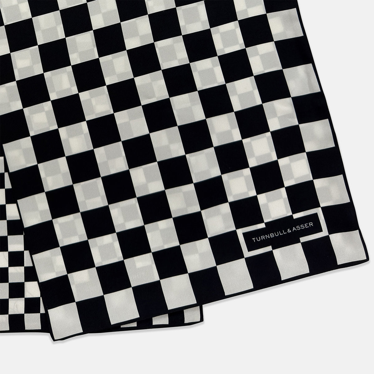 View 3 of product A Chequered Navy & White Scarf in Silk by Turnbull & Asser UK is displayed against a plain white background, showcasing its long, luxurious silk fabric with a striking navy and white checkered pattern.