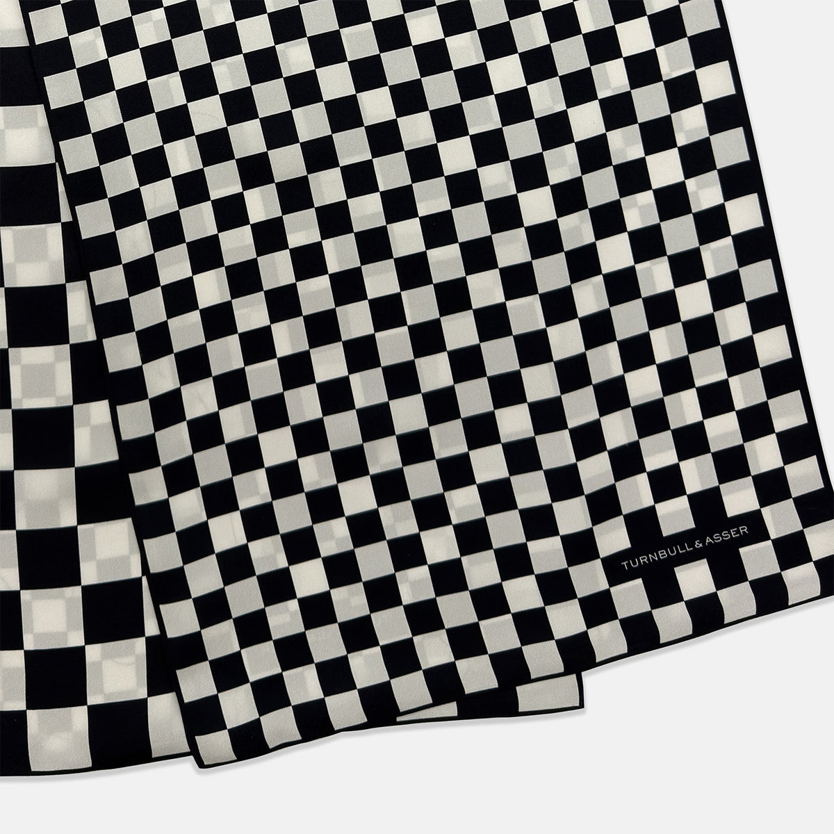 View 4 of product A Chequered Navy & White Scarf in Silk by Turnbull & Asser UK is displayed against a plain white background, showcasing its long, luxurious silk fabric with a striking navy and white checkered pattern.