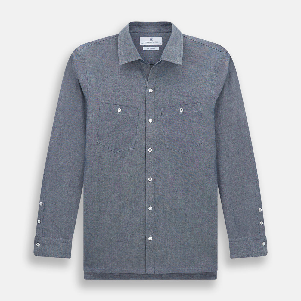 The Turnbull & Asser Steel Blue Piccadilly Shirt features long sleeves, a button-up front, two chest pockets, and white buttons, shown against a plain white background.