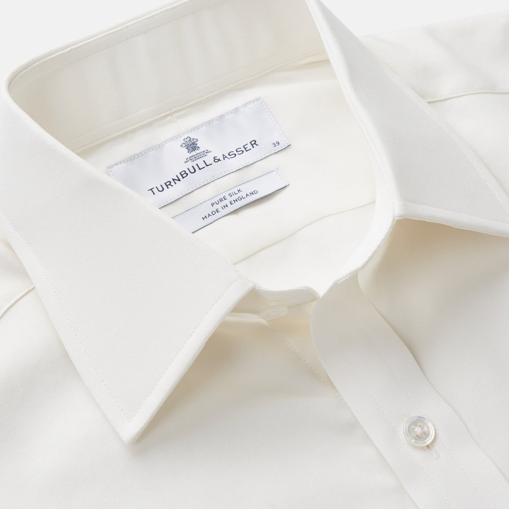 The Turnbull & Asser Cream Silk Mayfair Shirt features long sleeves, a classic collar, button-down front, and buttoned cuffs, shown laid flat on a white background.