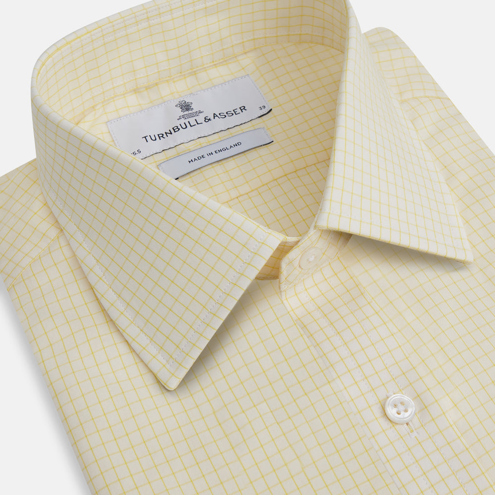 The Turnbull & Asser Yellow Graph Check Mayfair Shirt features long sleeves, a button-up front, and classic T&A collar in organic cotton with a light yellow check pattern—a summer staple shown on a plain white background.