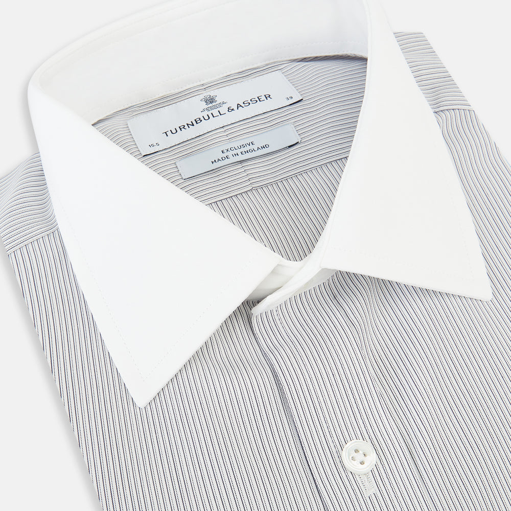 A navy men’s dress shirt with subtle white stripes, crafted from cotton and laid flat on a plain white background; the Striped White on Navy Regular Fit Shirt by Turnbull & Asser UK is a timeless formal piece for any wardrobe.