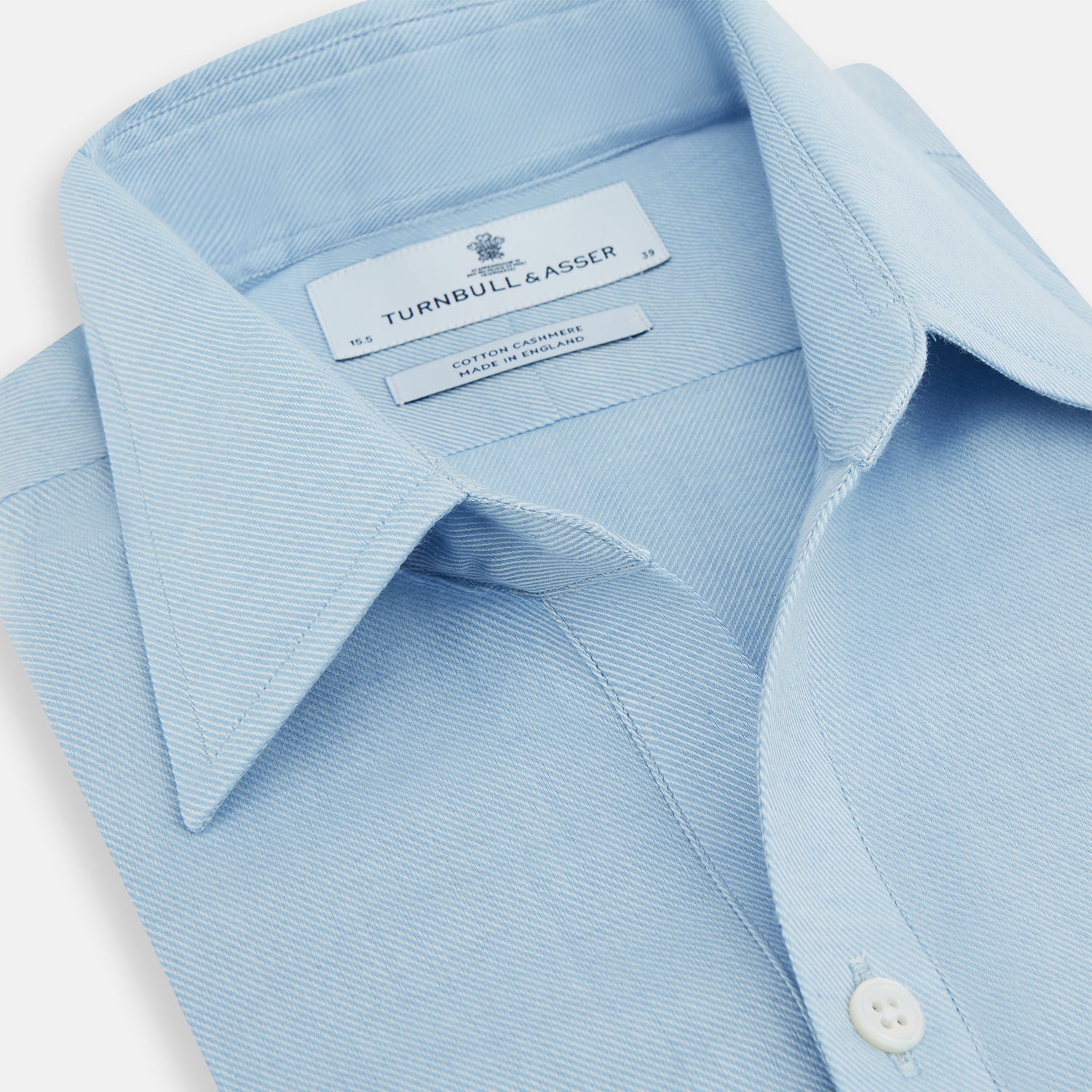 View 2 of product The Blue Cotton Cashmere Chelsea Shirt by Turnbull & Asser, a light blue long-sleeve button-up with a chest pocket, crafted from soft cotton and cashmere, is shown laid flat on a white background.