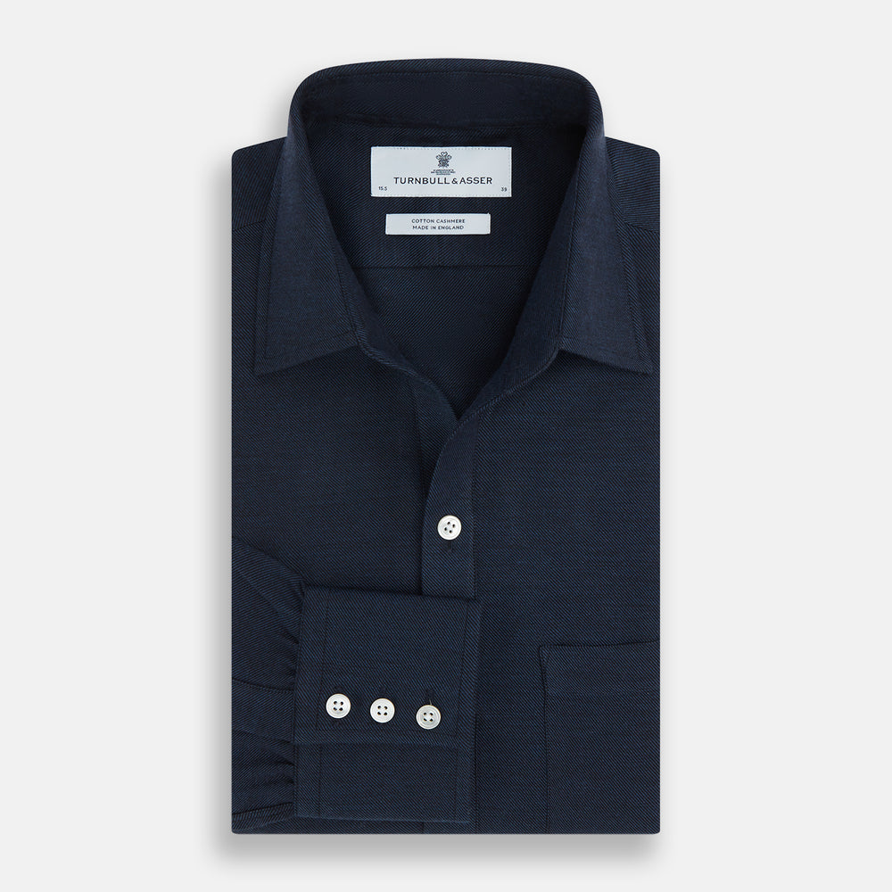 The Turnbull & Asser Navy Cotton Cashmere Chelsea Shirt features long sleeves, a classic collar, front chest pocket, and white buttons, shown laid flat on a white background.