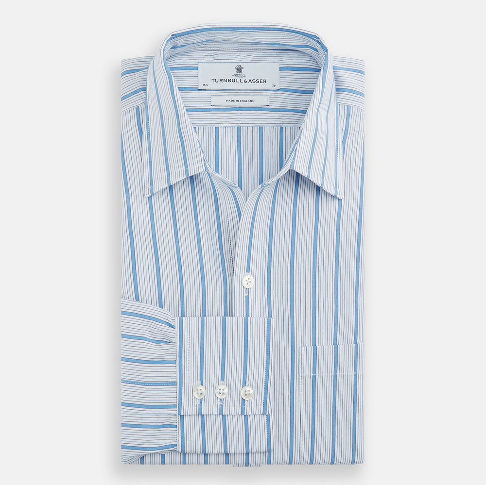 The Turnbull & Asser Blue Multi Track Stripe Chelsea Shirt features long sleeves, a light blue multi-stripe design, a chest pocket, open collar, and buttoned cuffs, shown laid flat on a white background.
