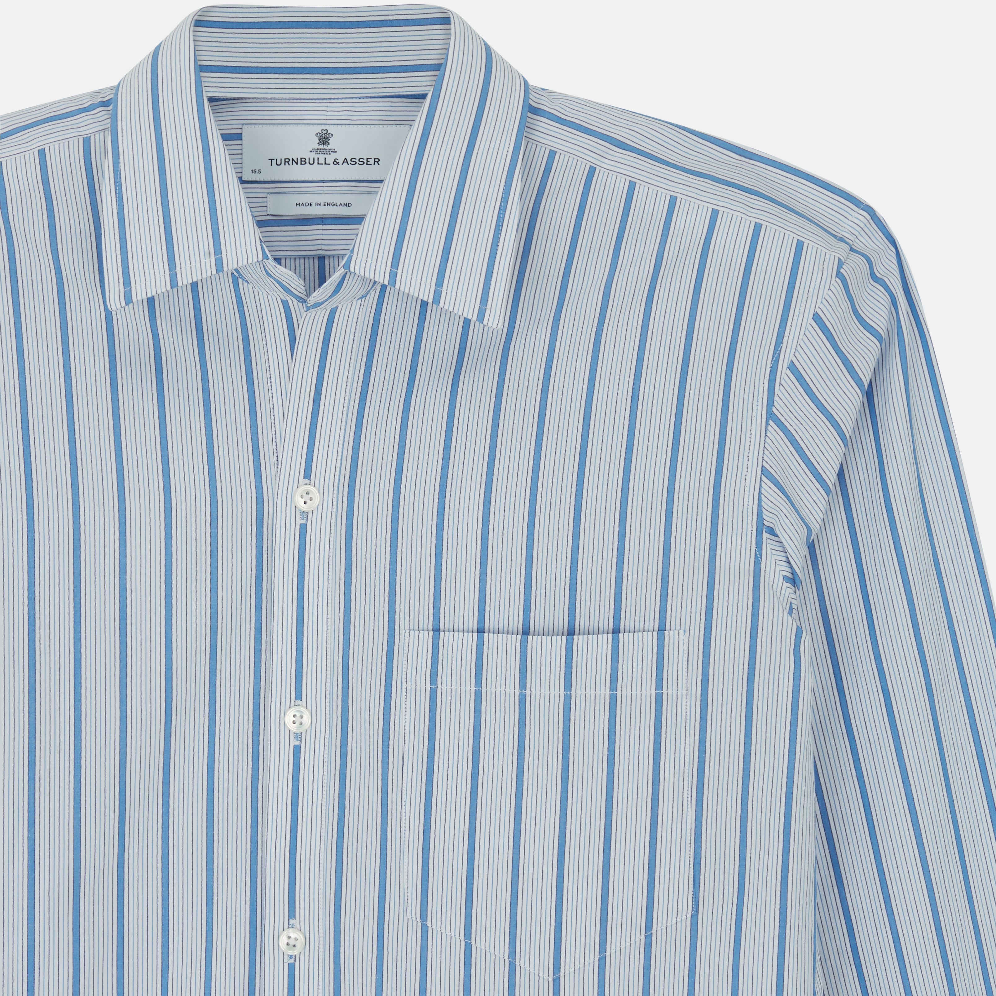 View 4 of product The Turnbull & Asser Blue Multi Track Stripe Chelsea Shirt features long sleeves, a light blue multi-stripe design, a chest pocket, open collar, and buttoned cuffs, shown laid flat on a white background.