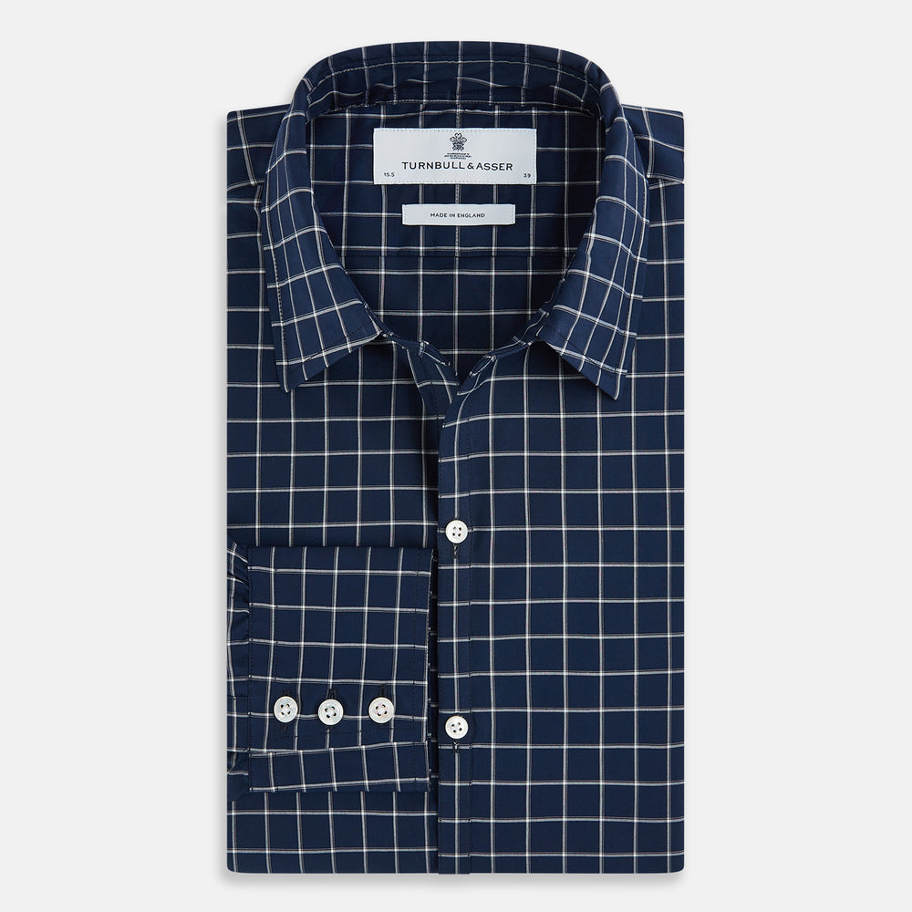 The Turnbull & Asser UK White Check on Navy Windsor Shirt features an open collar, button cuffs, and cuffed long sleeves. Showcased against a white background, this shirt presents a navy base adorned with a white grid pattern.