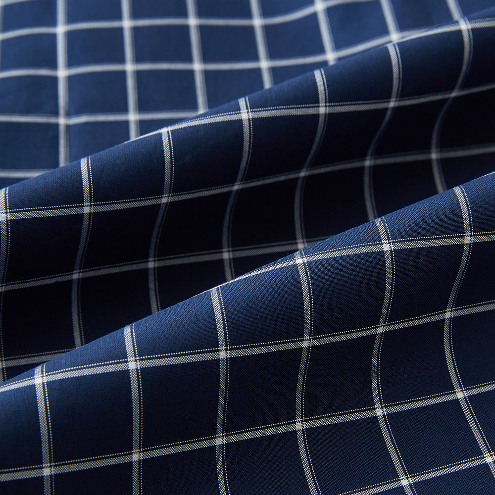 The Turnbull & Asser UK White Check on Navy Windsor Shirt features an open collar, button cuffs, and cuffed long sleeves. Showcased against a white background, this shirt presents a navy base adorned with a white grid pattern.