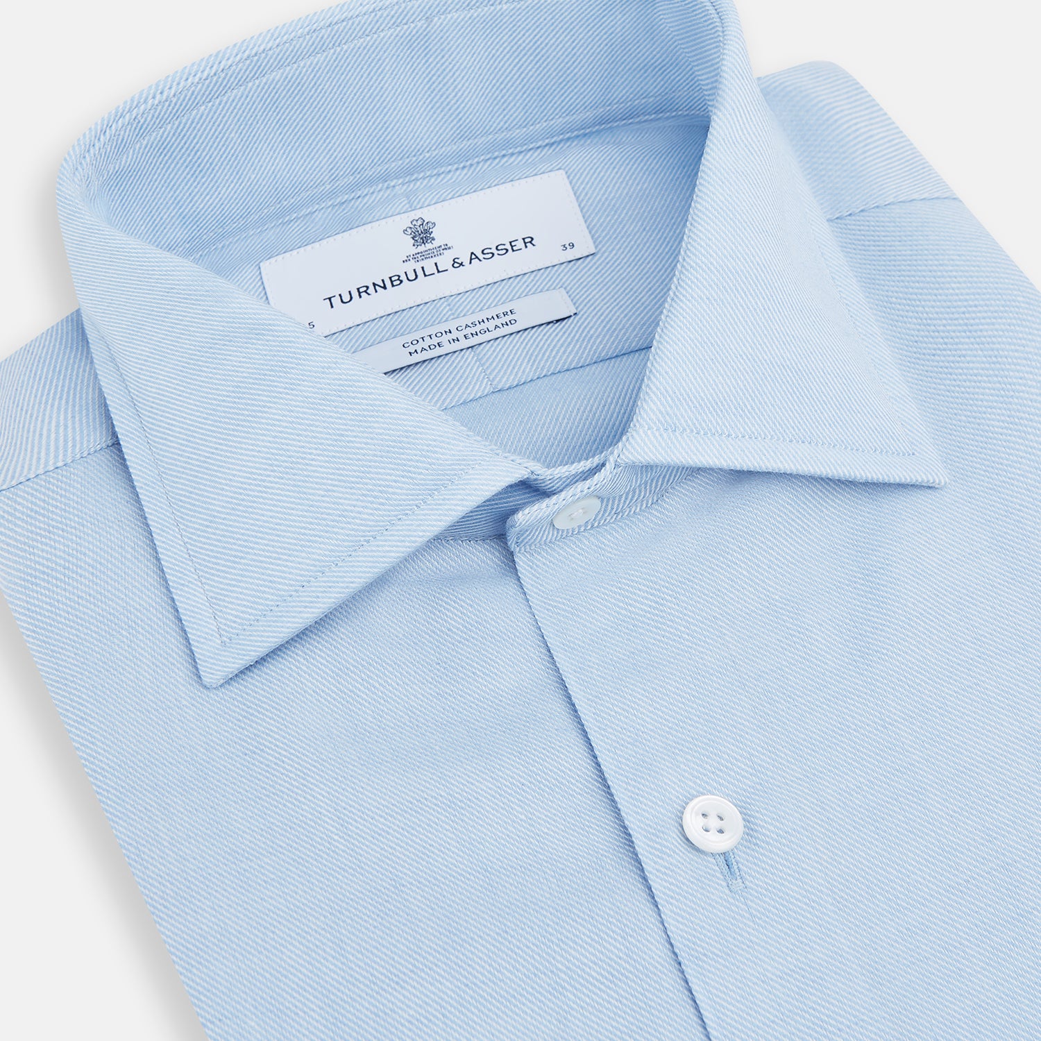 View 2 of product The Turnbull & Asser Tailored Fit Blue Cotton Cashmere Belgravia Shirt features a classic collar, button-down front, and buttoned cuffs, shown laid flat on a white background for a refined, formal look.