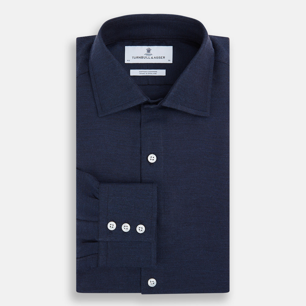 The Turnbull & Asser Tailored Fit Navy Cotton Cashmere Belgravia Shirt features a classic collar, white buttons, and long sleeves, shown on a white background.