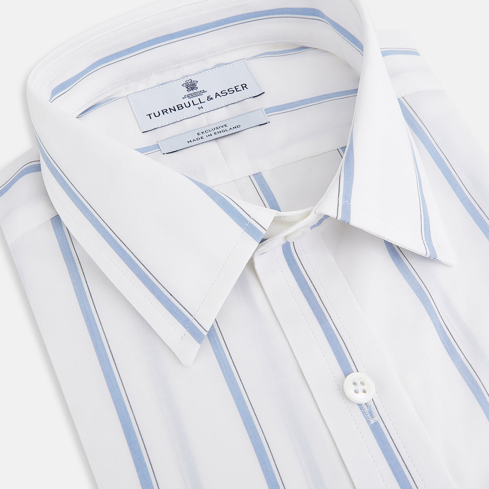 The Turnbull & Asser UK Track Striped Blue on White Weekend Fit Shirt in Cotton is a long-sleeve, button-up shirt featuring blue stripes on premium white Italian cotton, a Derby collar, and a chest pocket, elegantly laid flat against a white background.