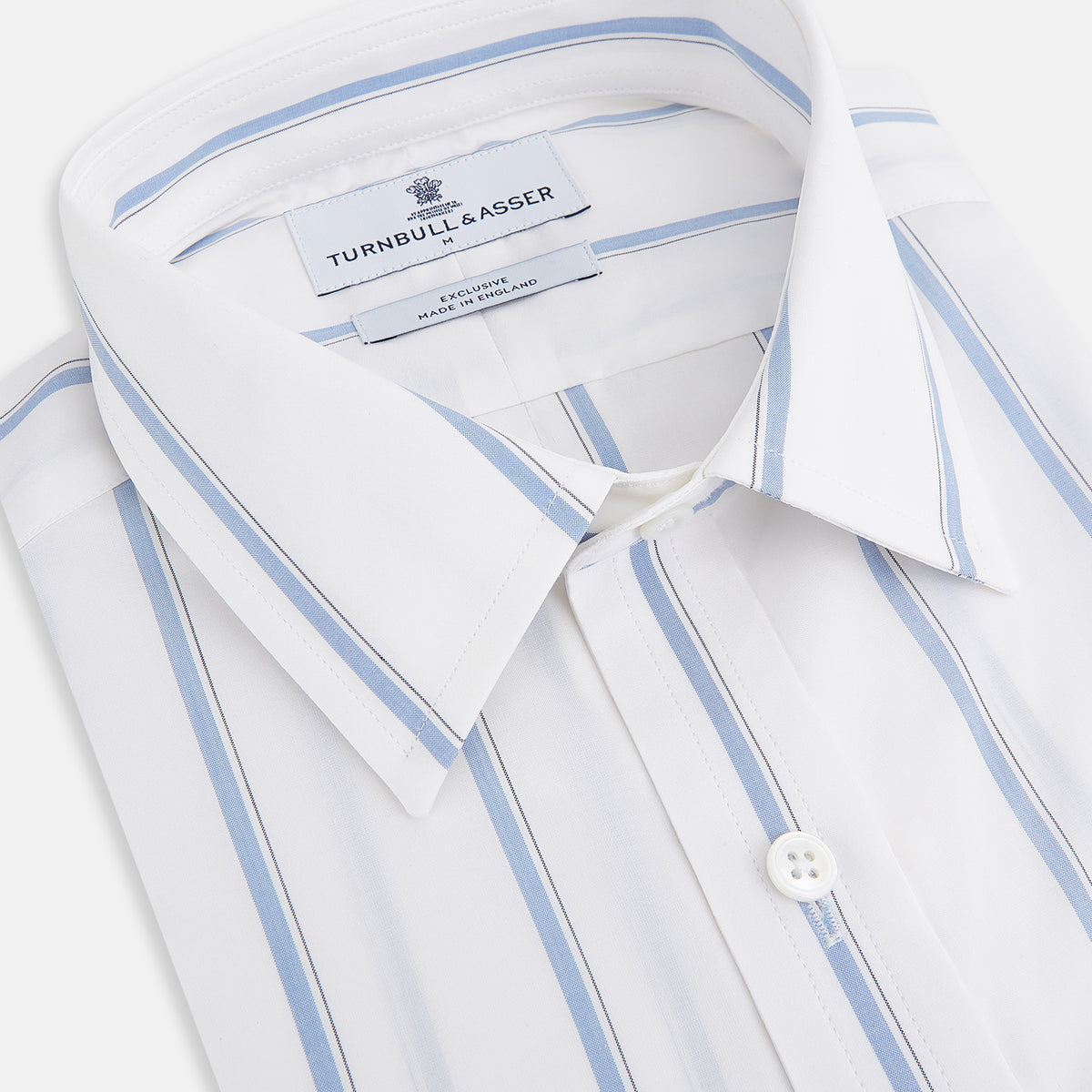 View 2 of product The Turnbull & Asser UK Track Striped Blue on White Weekend Fit Shirt in Cotton is a long-sleeve, button-up shirt featuring blue stripes on premium white Italian cotton, a Derby collar, and a chest pocket, elegantly laid flat against a white background.
