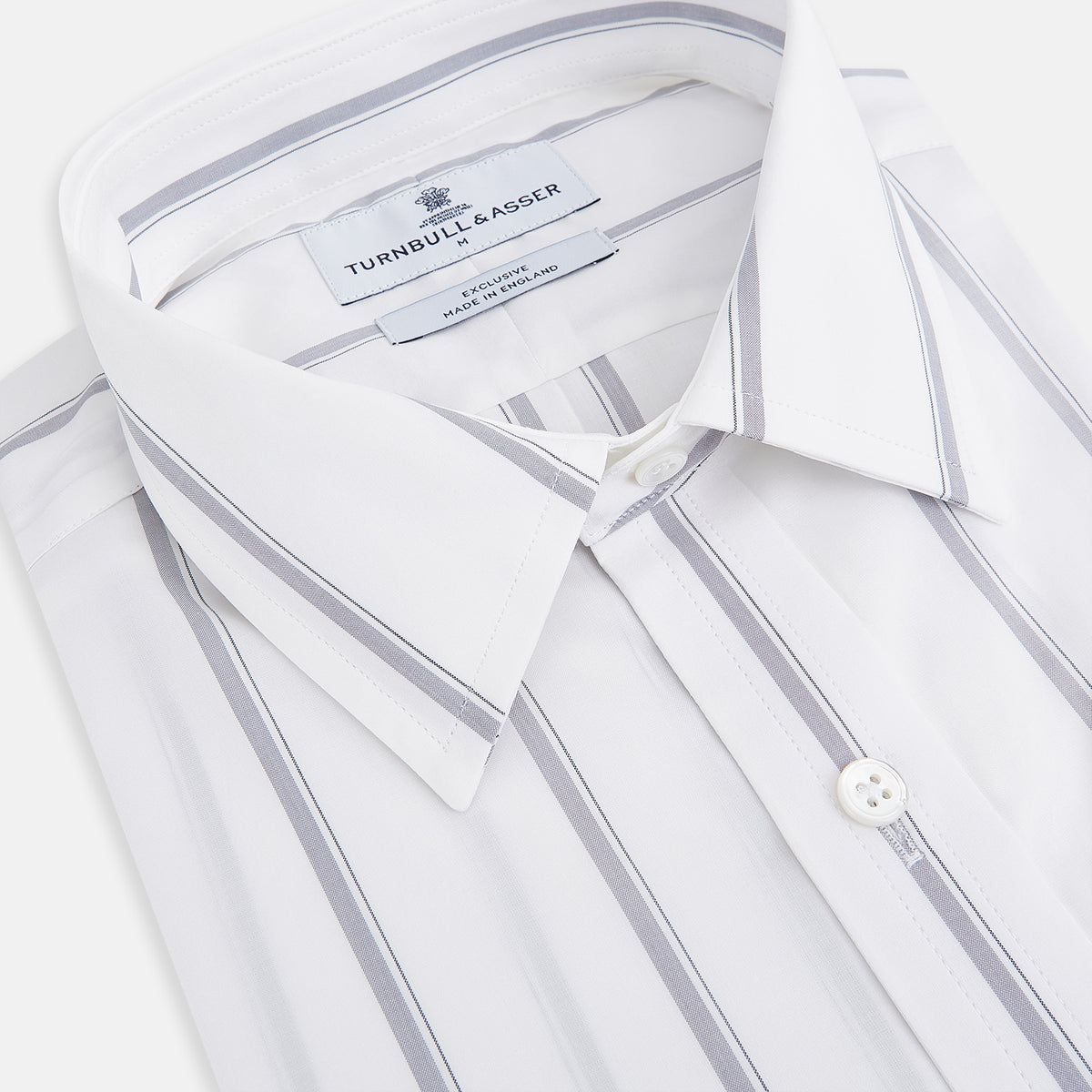 View 2 of product Introducing the Track Striped Grey on White Weekend Fit Shirt in Cotton by Turnbull & Asser UK—a men’s long-sleeve dress shirt crafted from crisp white cotton, featuring vertical grey stripes, a button-down front, derby collar, cuffs, and a chest pocket. The shirt is displayed laid flat on a white surface.