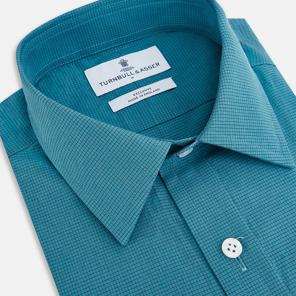 Here’s a rewritten version using your product data: The Turnbull & Asser UK Fine Checked Turquoise Blue Weekend Fit Shirt in Cotton is a men’s long-sleeve button-up, featuring a chest pocket, white buttons, and a pointed collar, shown laid flat against a white background.