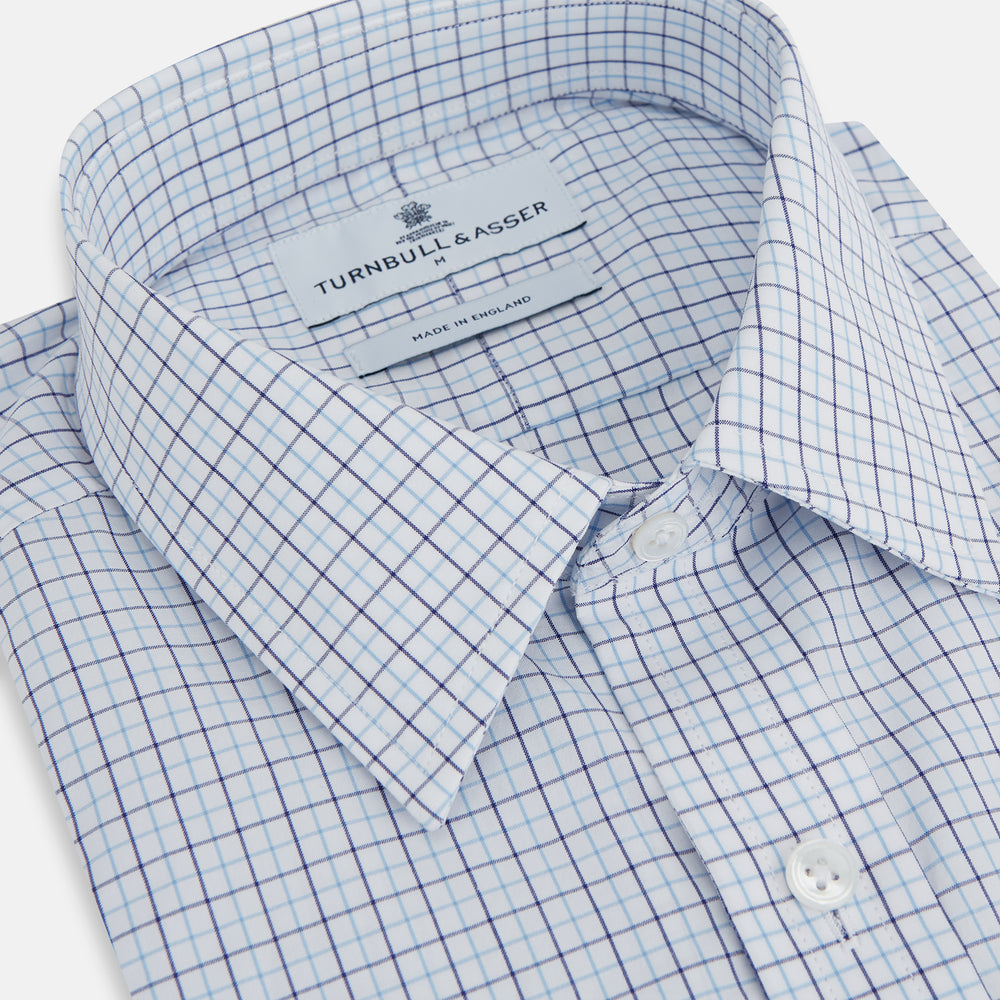 The Turnbull & Asser Blue Double Graph Check Richmond Shirt features a light blue and white check pattern, front pocket, Derby collar, buttoned cuffs, and long sleeves, shown laid flat on a white background.