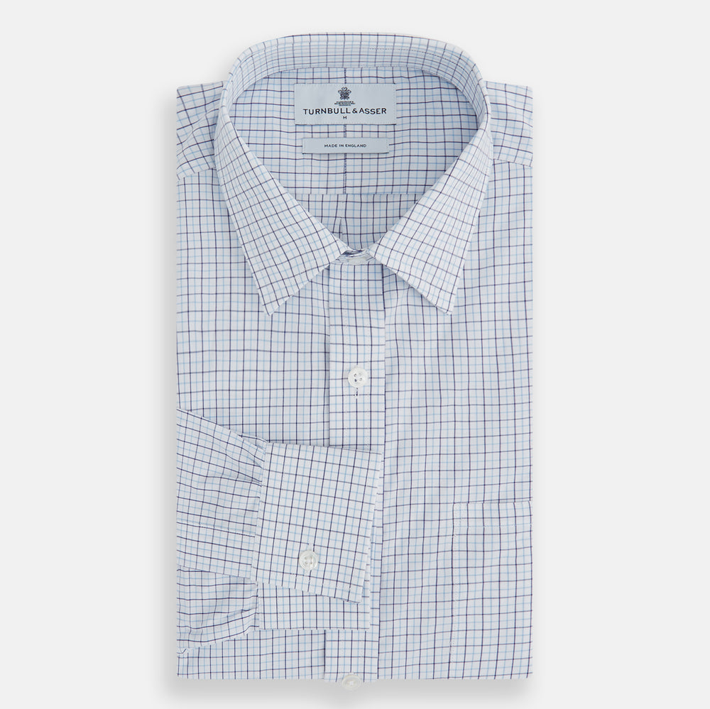 The Turnbull & Asser Blue Double Graph Check Richmond Shirt features a light blue and white check pattern, front pocket, Derby collar, buttoned cuffs, and long sleeves, shown laid flat on a white background.