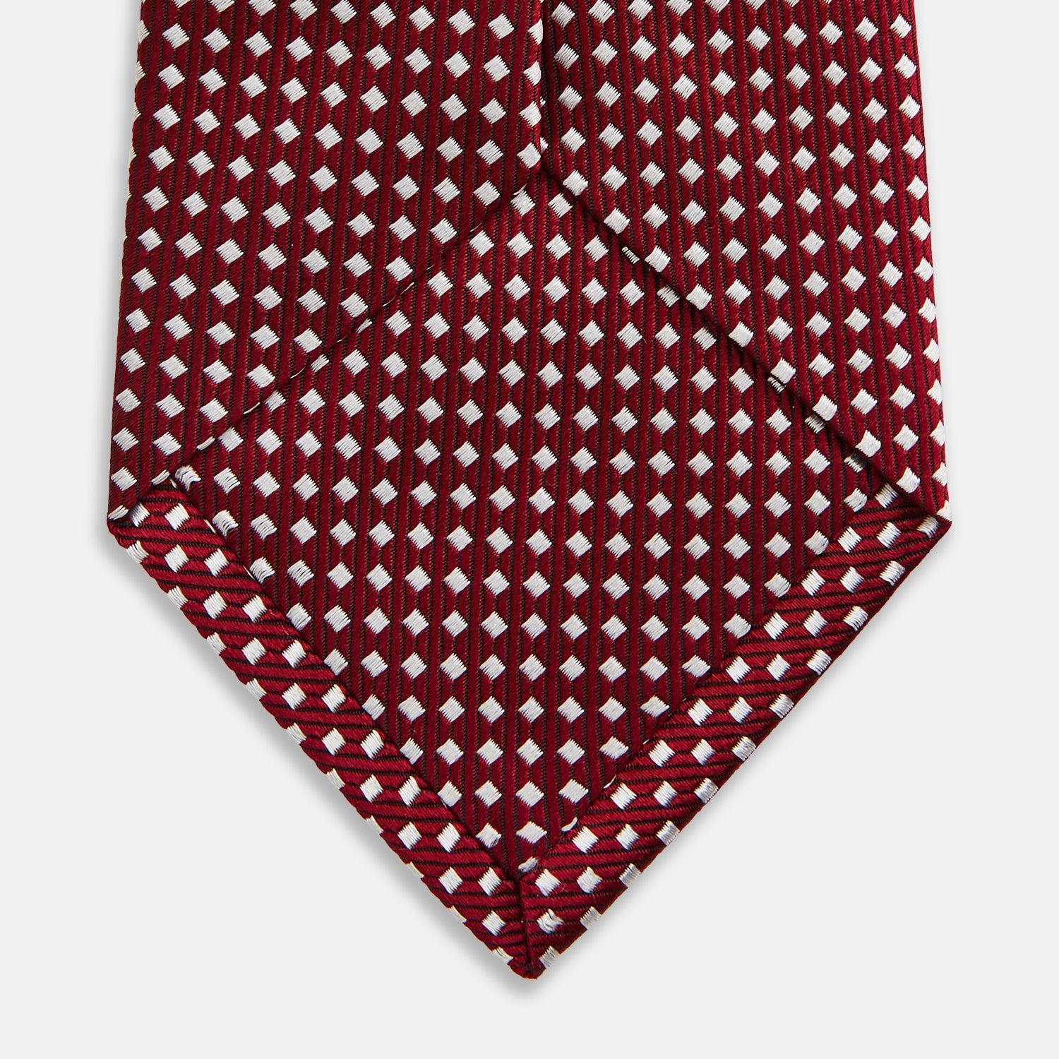 View 4 of product The Turnbull & Asser Slim Burgundy and White Diamond Silk Tie, shown rolled on a white background, features a repeating pattern of small white diamonds—an ideal accessory to complement any office shirt.